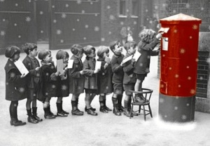 Imagen de épocas pasadas donde varios niños hacen cola para depositar su carta en un buzón tradicional.